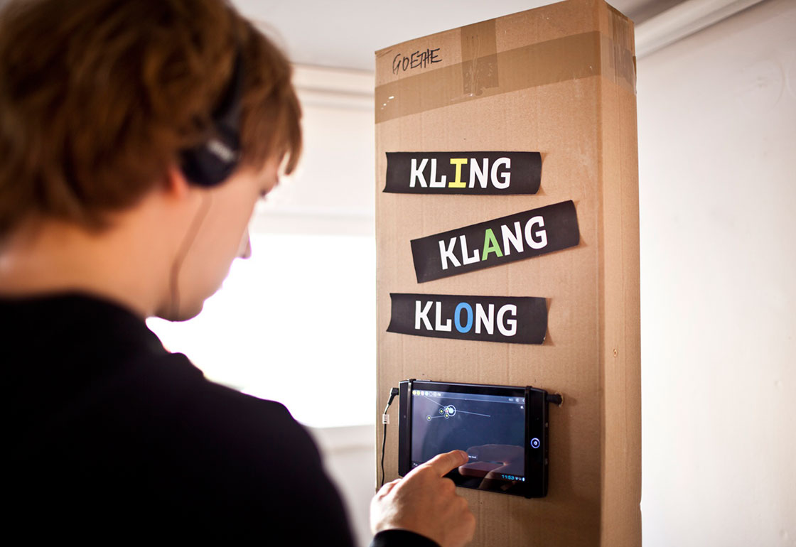 Person with headphones on touching a tablet with Kling Klang Klong sign above