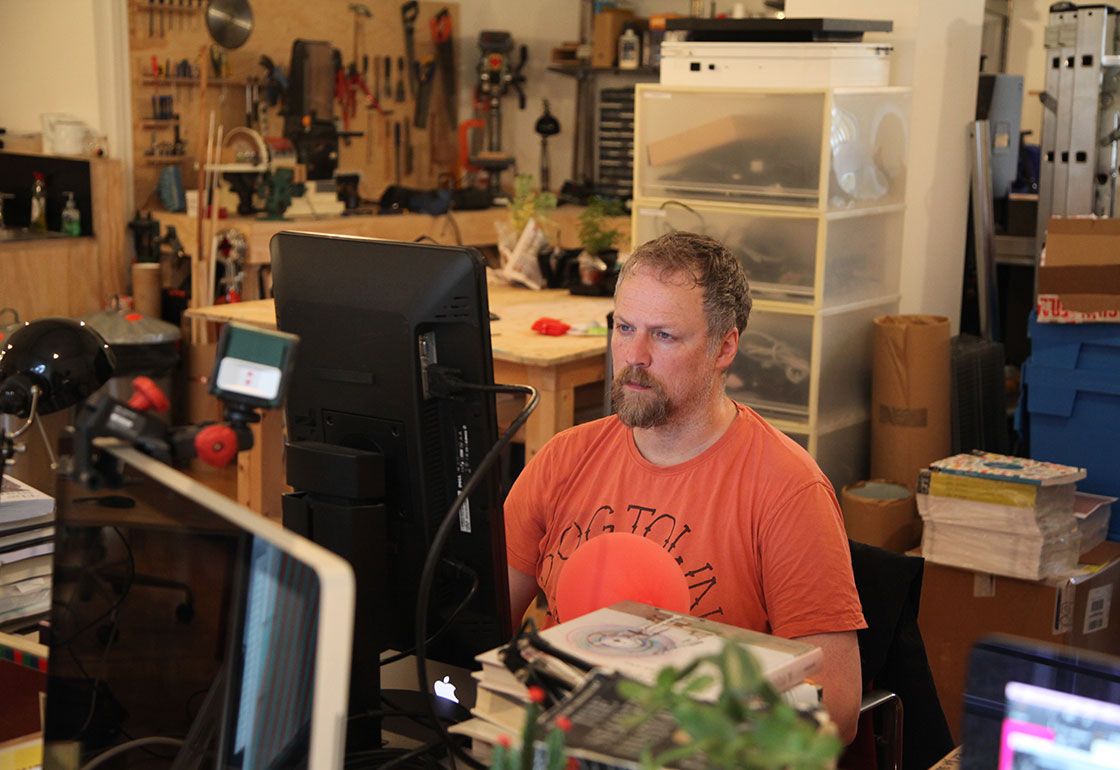 Michael Straubig in the Kin studio sitting at a desk with workshop in the background