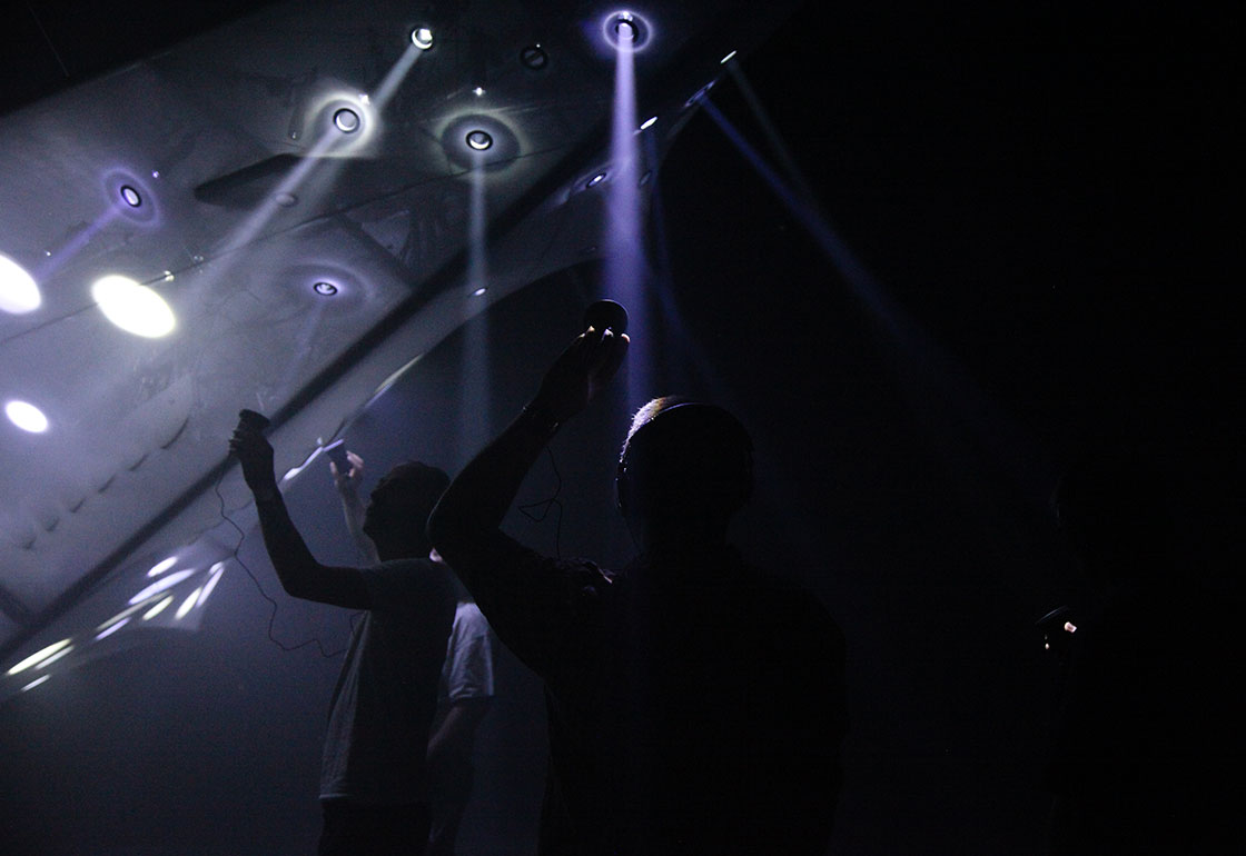 A dark room with people looking at lights in the shape of a plane
